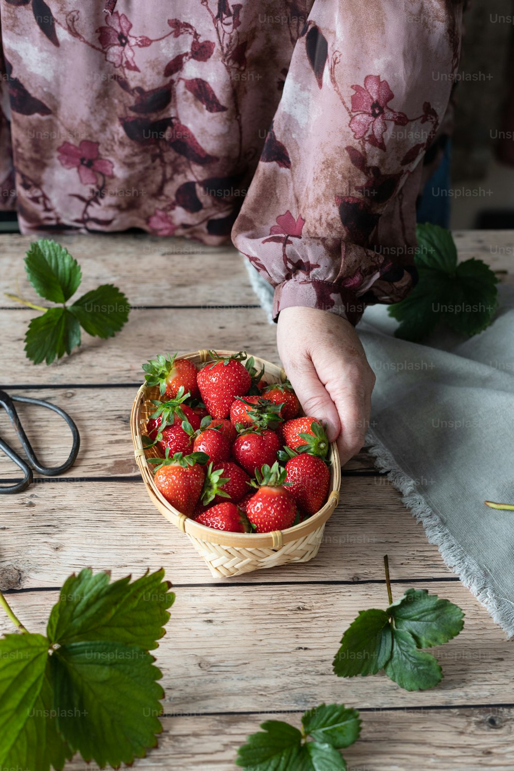 eine Person, die Erdbeeren aus einem Korb auf einem Tisch pflückt