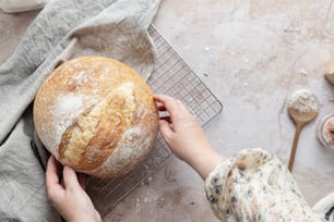 a person holding a loaf of bread over a cooling rack