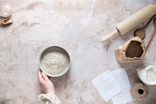 a person holding a bowl of flour next to a rolling pin