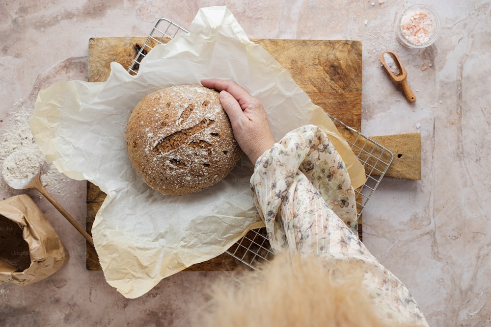 a person holding a loaf of bread on top of a wooden cutting board