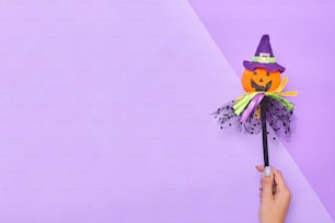 eine Hand, die eine Halloween-Dekoration auf einem lila Hintergrund hält