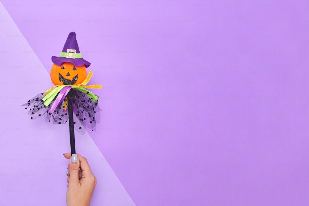 une main tenant un chapeau de sorcière en papier sur un mur violet