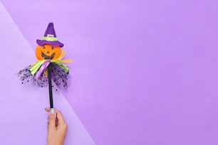 Una mano sosteniendo un sombrero de bruja de papel encima de una pared púrpura