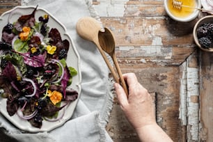 a person holding a wooden spoon over a plate of salad