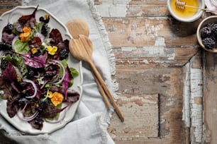 a white plate topped with a salad next to a wooden spoon