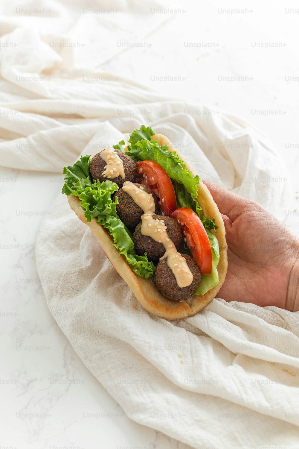 a hand holding a sandwich with meat, lettuce and tomatoes