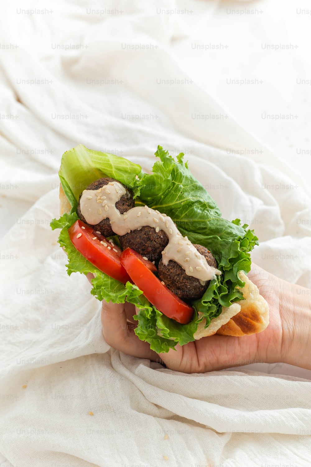 a hand holding a sandwich with lettuce and tomatoes