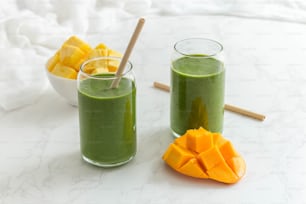 Deux verres de smoothie vert à côté d’un bol de tranches de mangue