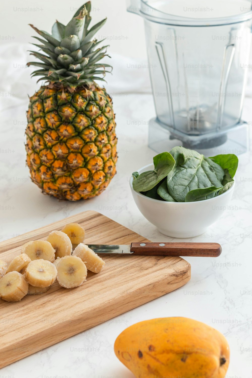 a pineapple and bananas on a cutting board next to a blender