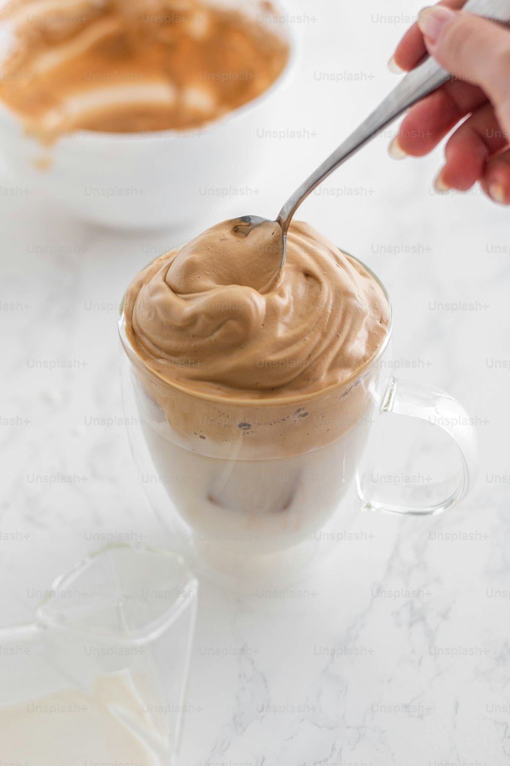 a hand holding a spoon over a cup of peanut butter