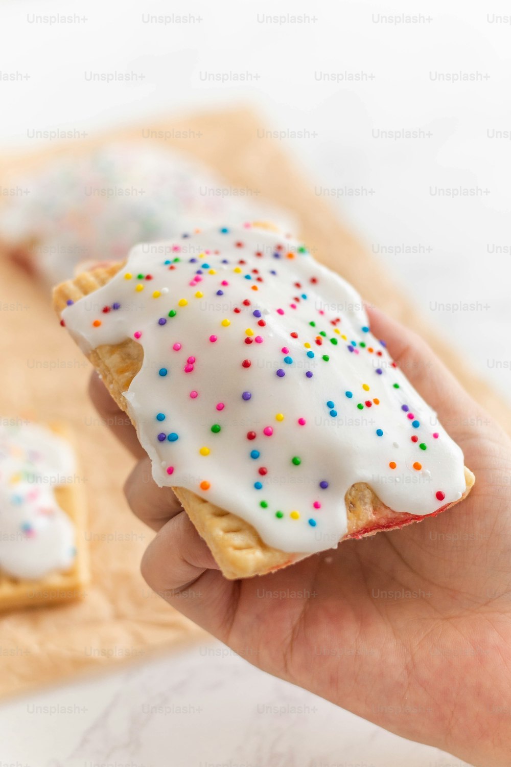 a hand holding a pastry with white frosting and sprinkles