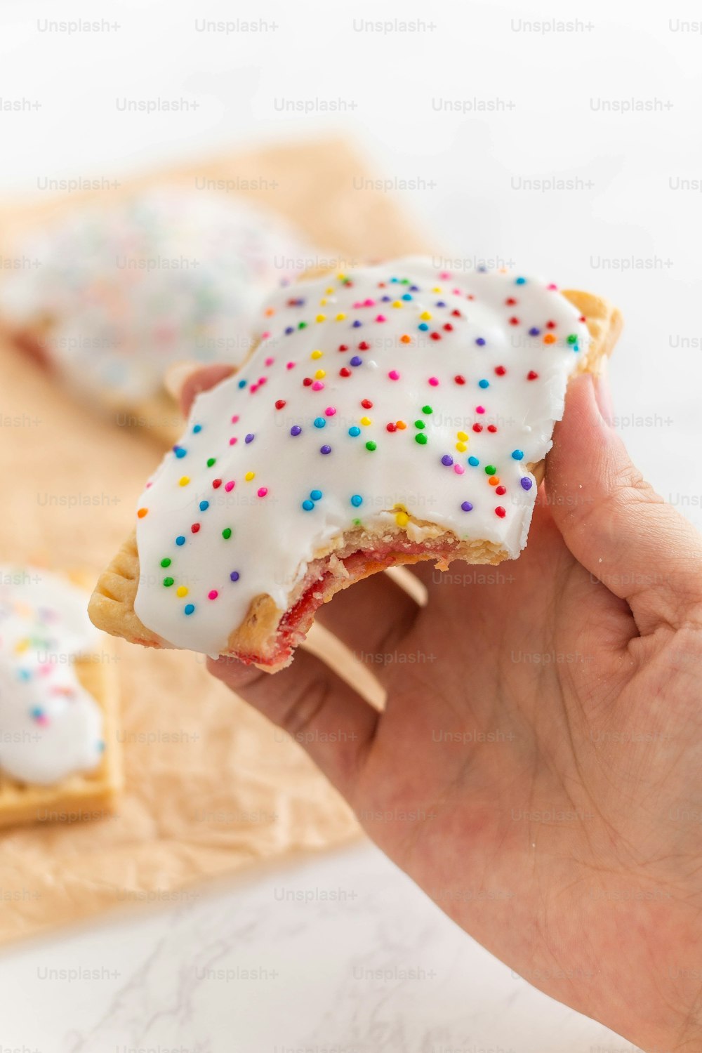 a hand holding a sprinkled donut on a toothpick