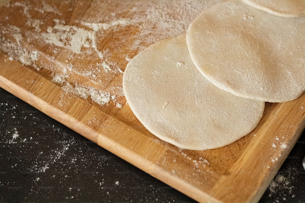 a wooden cutting board topped with three uncooked tortillas
