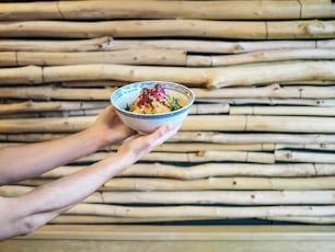 une personne tenant un bol de nourriture devant un mur de bambou