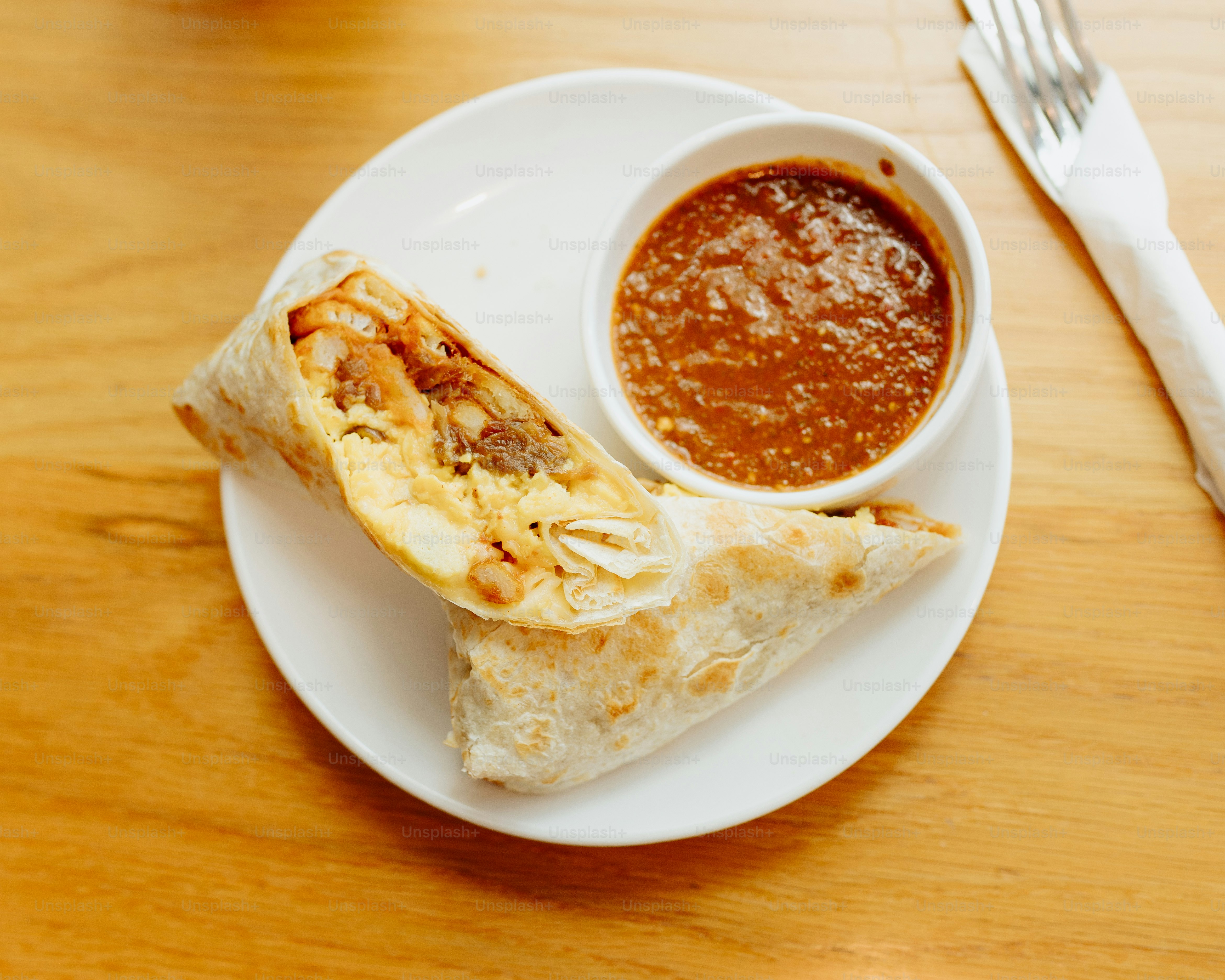 a white plate topped with a burrito and a bowl of salsa
