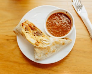 a white plate topped with a burrito and a bowl of salsa