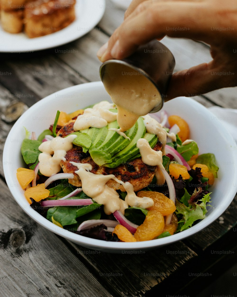 a person pouring dressing on a salad in a bowl