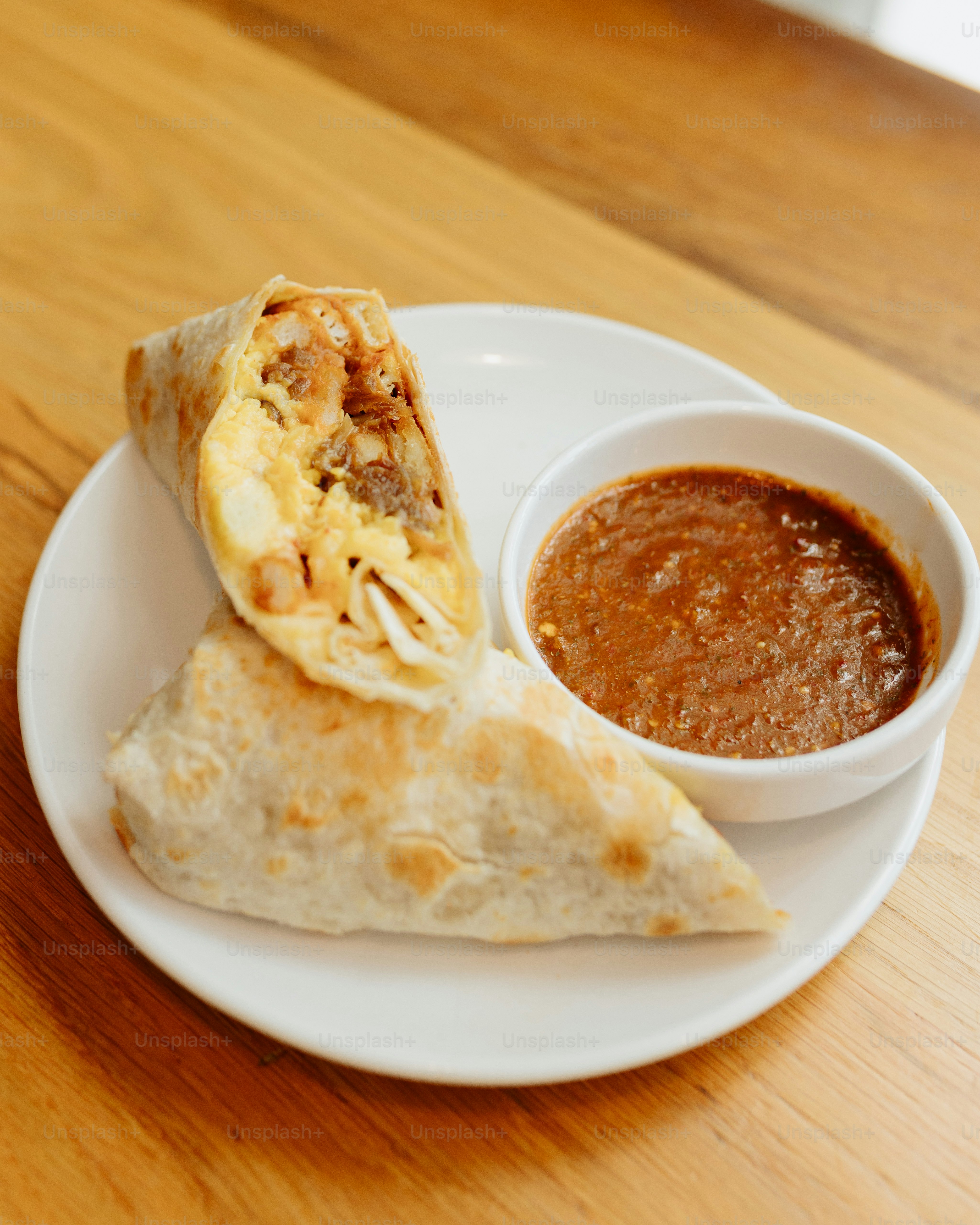 a burrito on a plate with a bowl of salsa