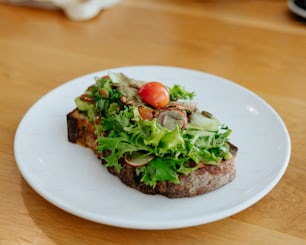 a white plate topped with a piece of meat covered in veggies