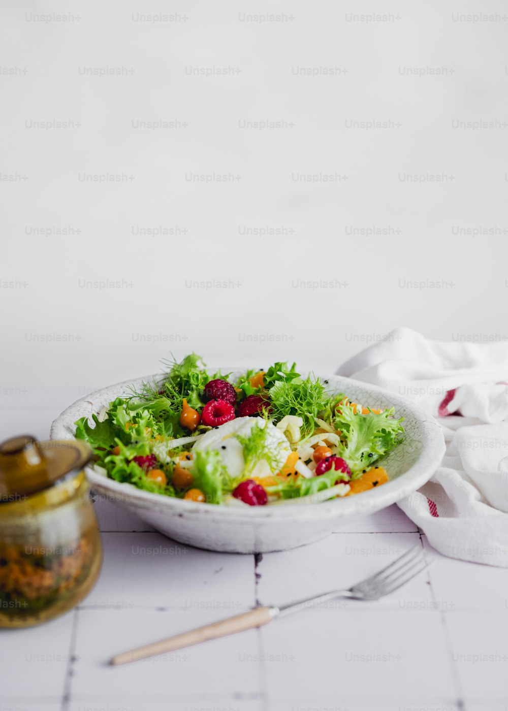 eine weiße Schüssel gefüllt mit einem Salat neben einer Gabel