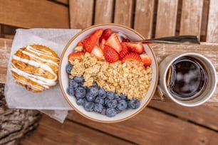 a bowl of cereal, strawberries, blueberries, and a donut