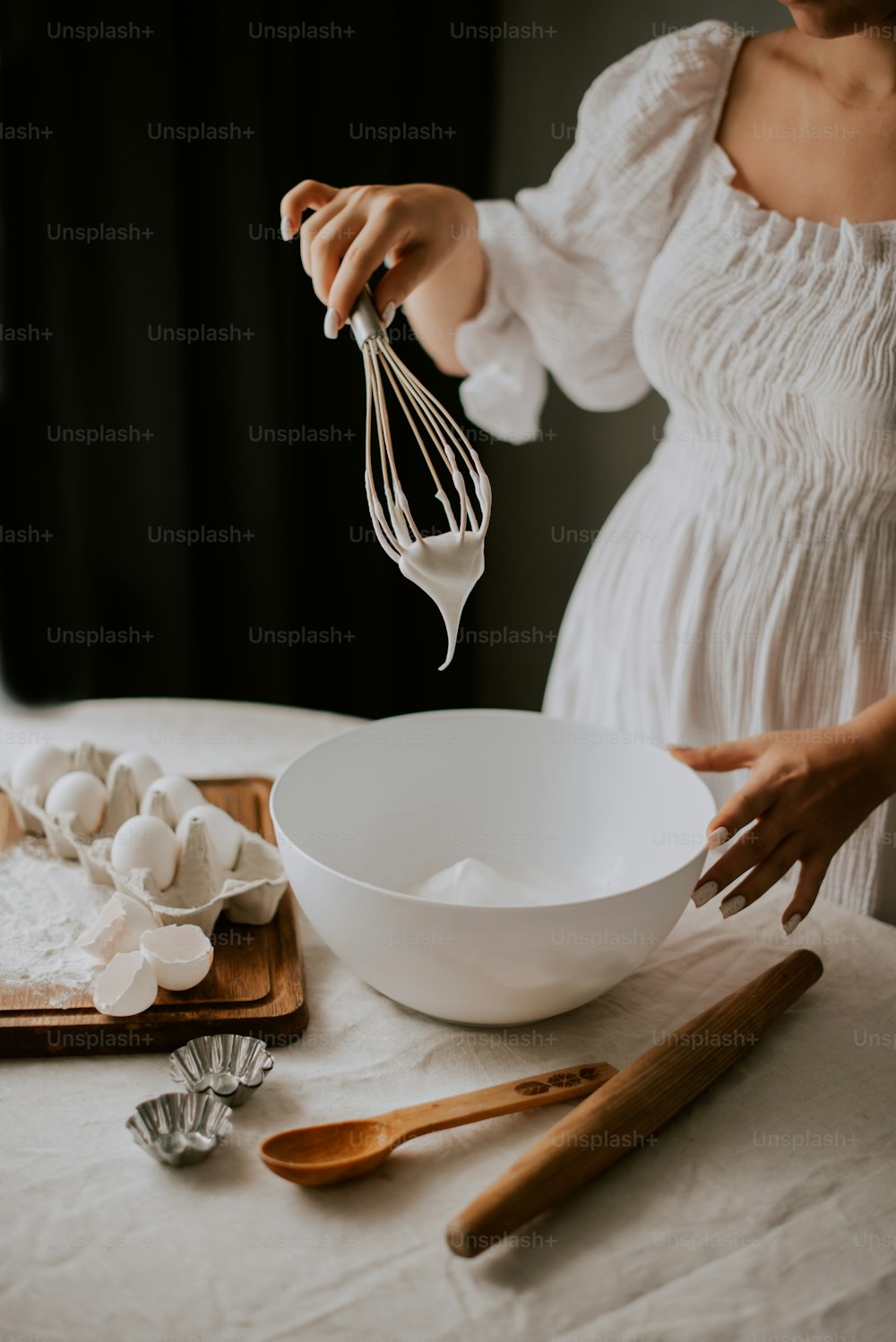 白いドレスを着た女性が卵をボウルに泡だて器で入れる