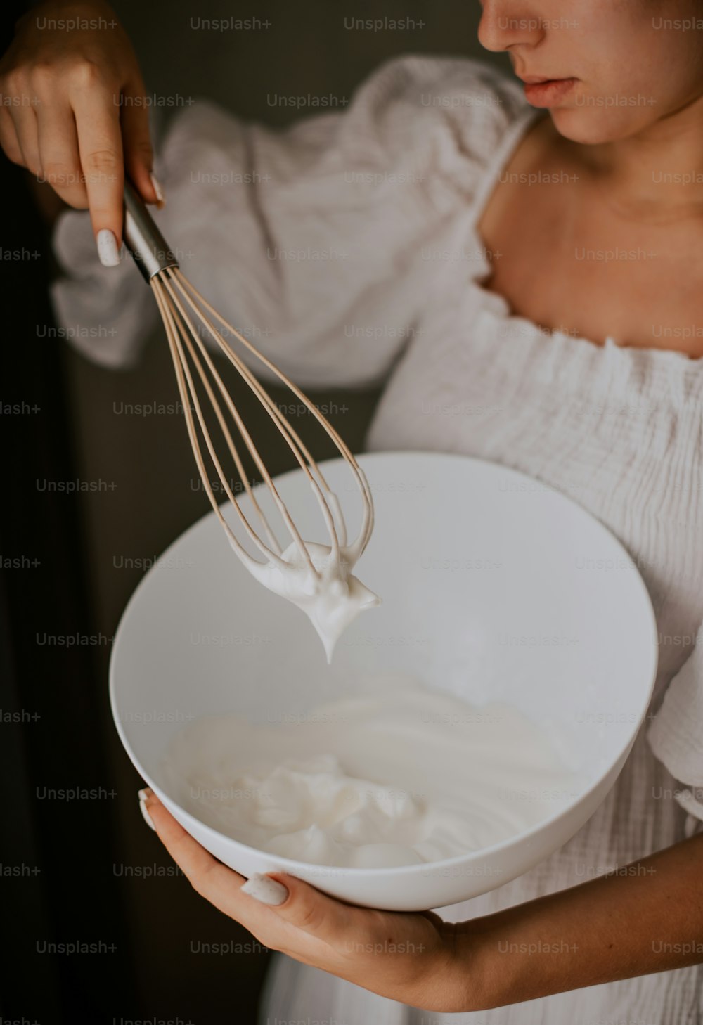 a woman holding a white bowl with a whisk in it