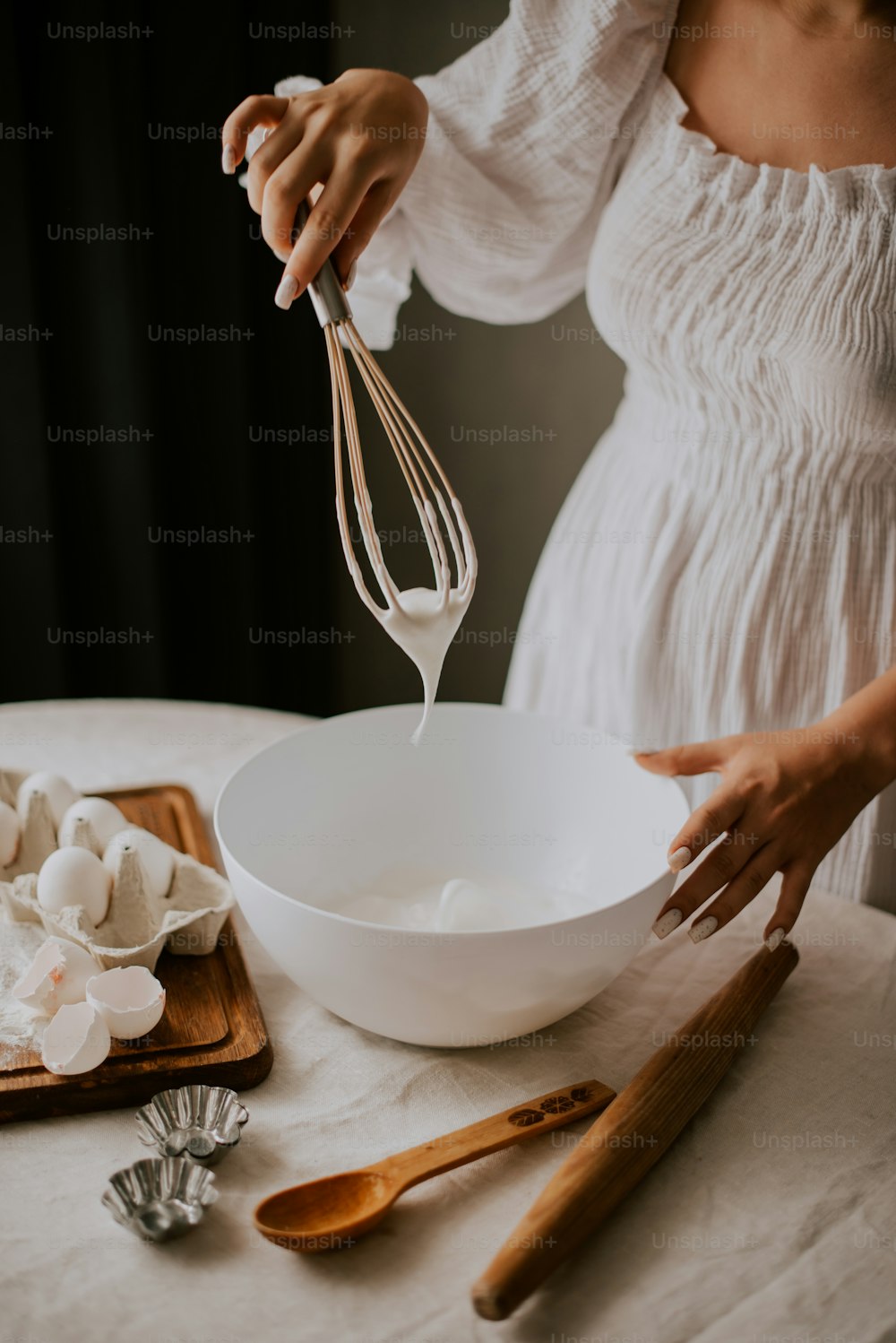 a woman in a white dress is whisking a bowl with a whis