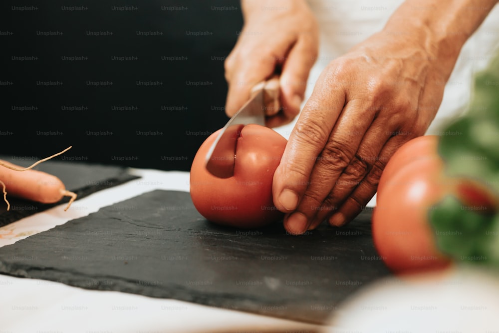 uma pessoa cortando um tomate em uma tábua de corte