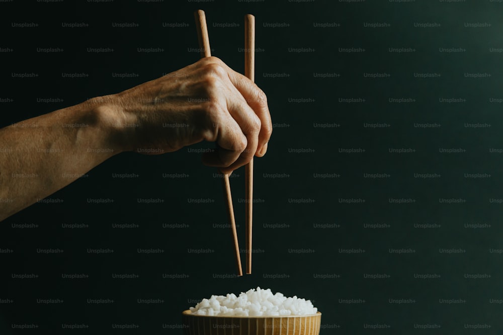 a person holding chopsticks over a bowl of rice