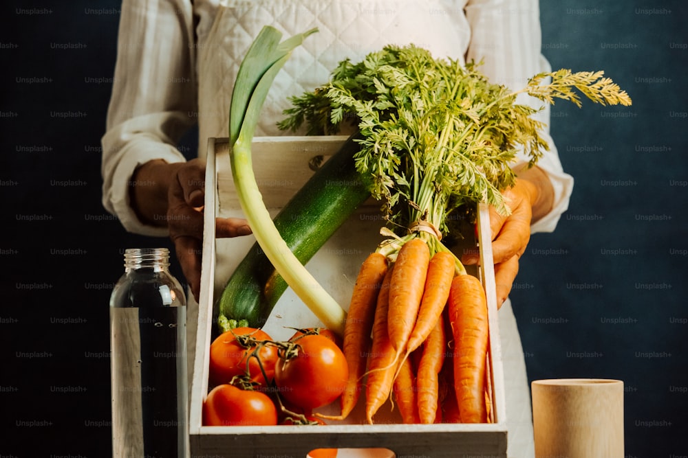 una persona sosteniendo una caja llena de verduras