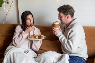 Un hombre y una mujer sentados en un sofá comiendo comida y bebiendo café