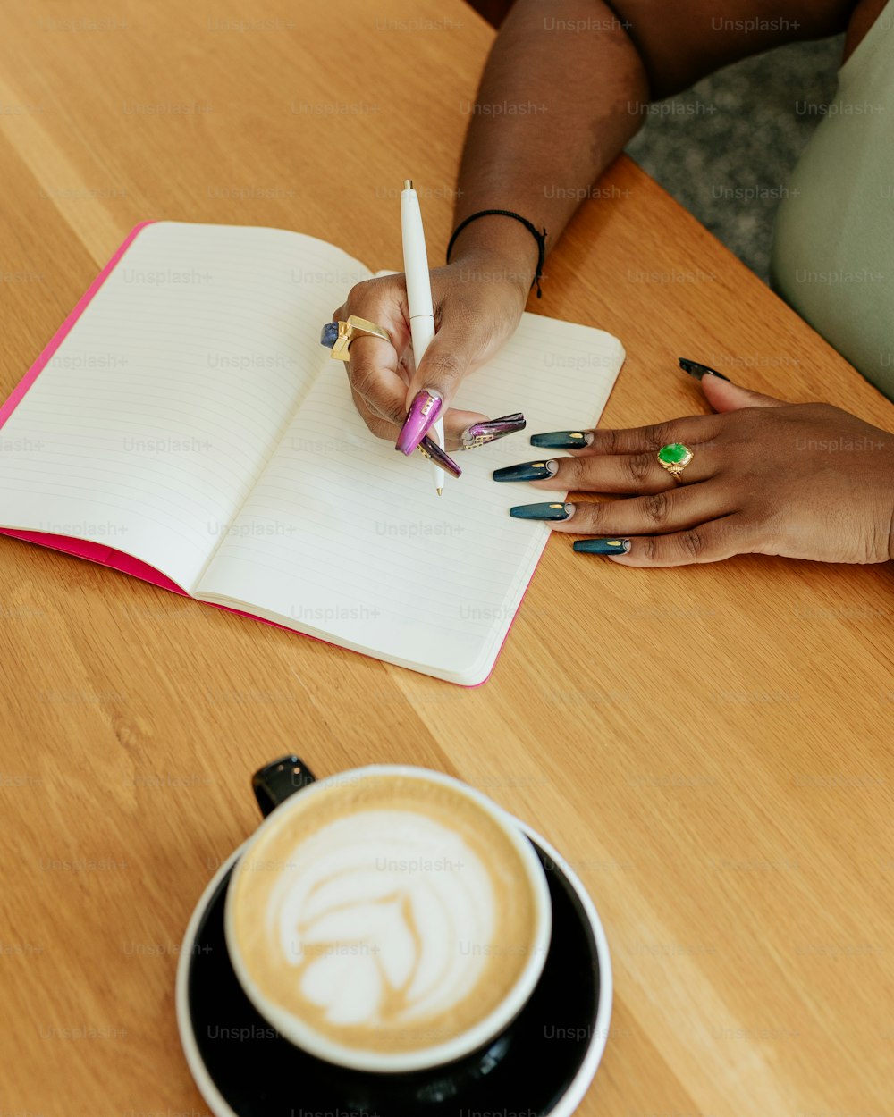 a person writing in a notebook on a table with a cup of coffee