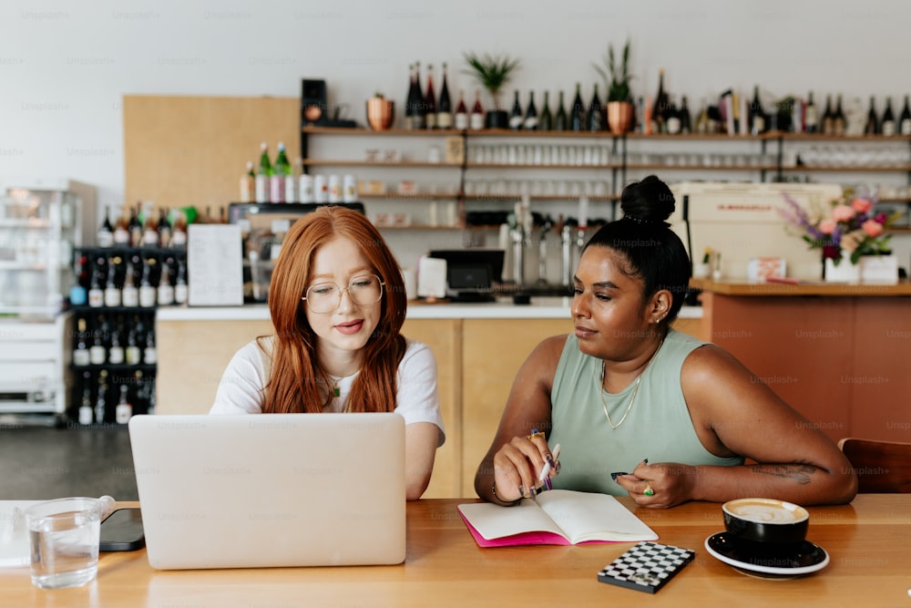 Dos mujeres sentadas en una mesa mirando una computadora portátil