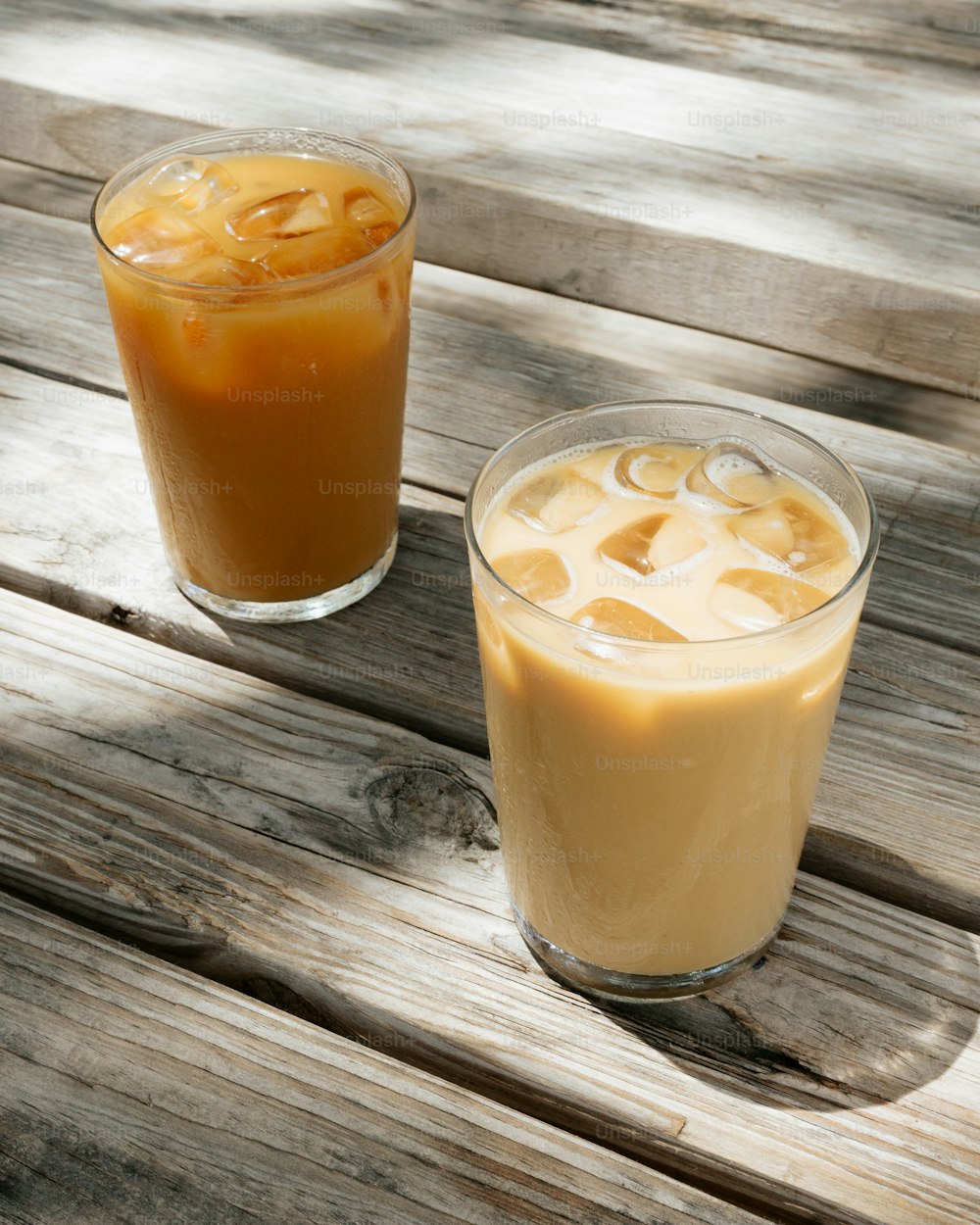 two glasses of iced coffee sitting on top of a wooden table