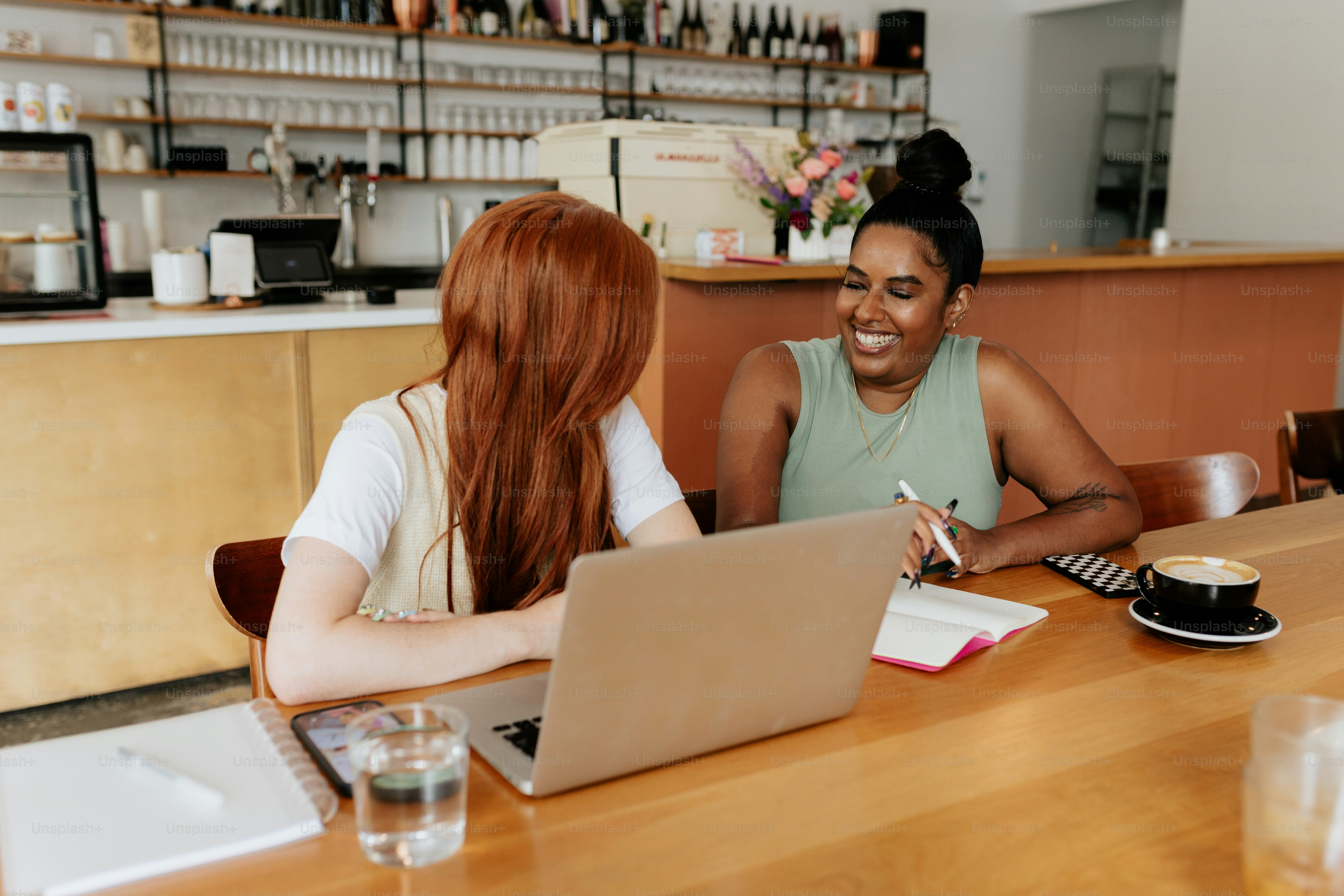 two women sitting at a table with a laptop