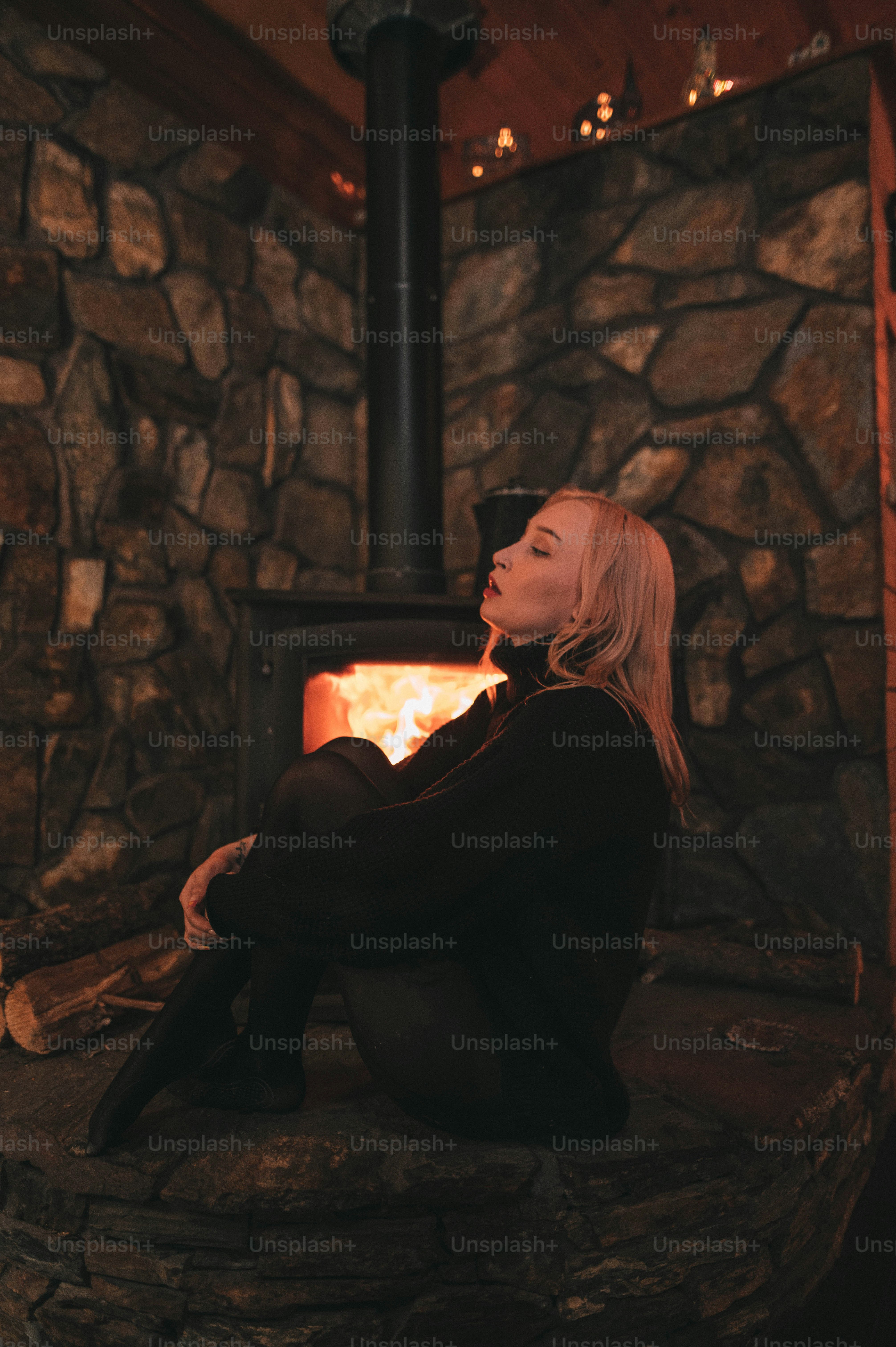A woman sitting in front of a wood burning stove photo – Log cabin ...