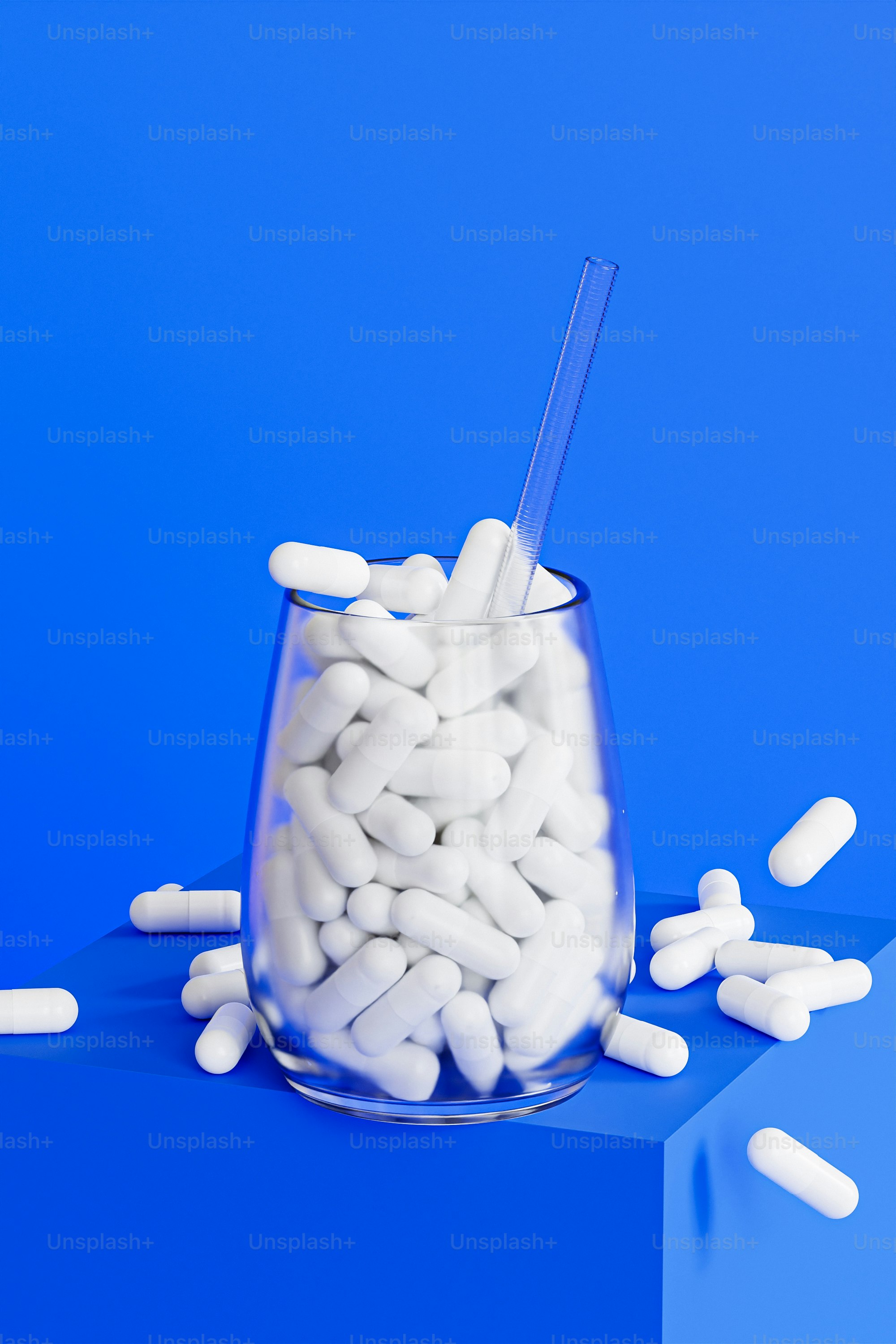 A glass filled with white pills sitting on top of a blue surface photo ...