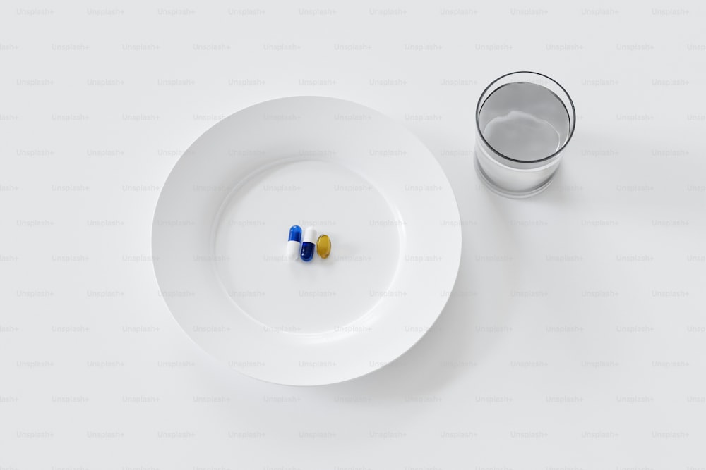 une assiette blanche avec deux pilules dessus à côté d’un verre d’eau