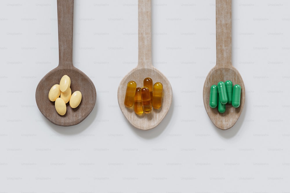 three wooden spoons with different colored pills in them
