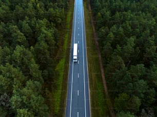 an aerial view of a truck driving down a road in the middle of a forest