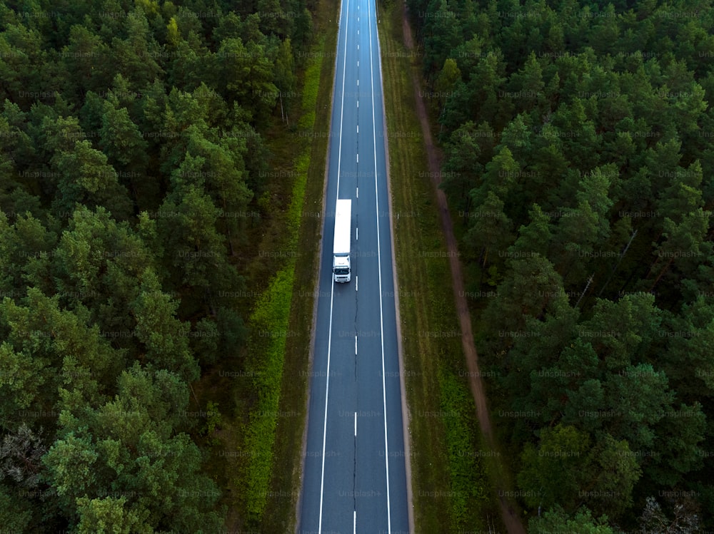 an aerial view of a truck driving down a road in the middle of a forest