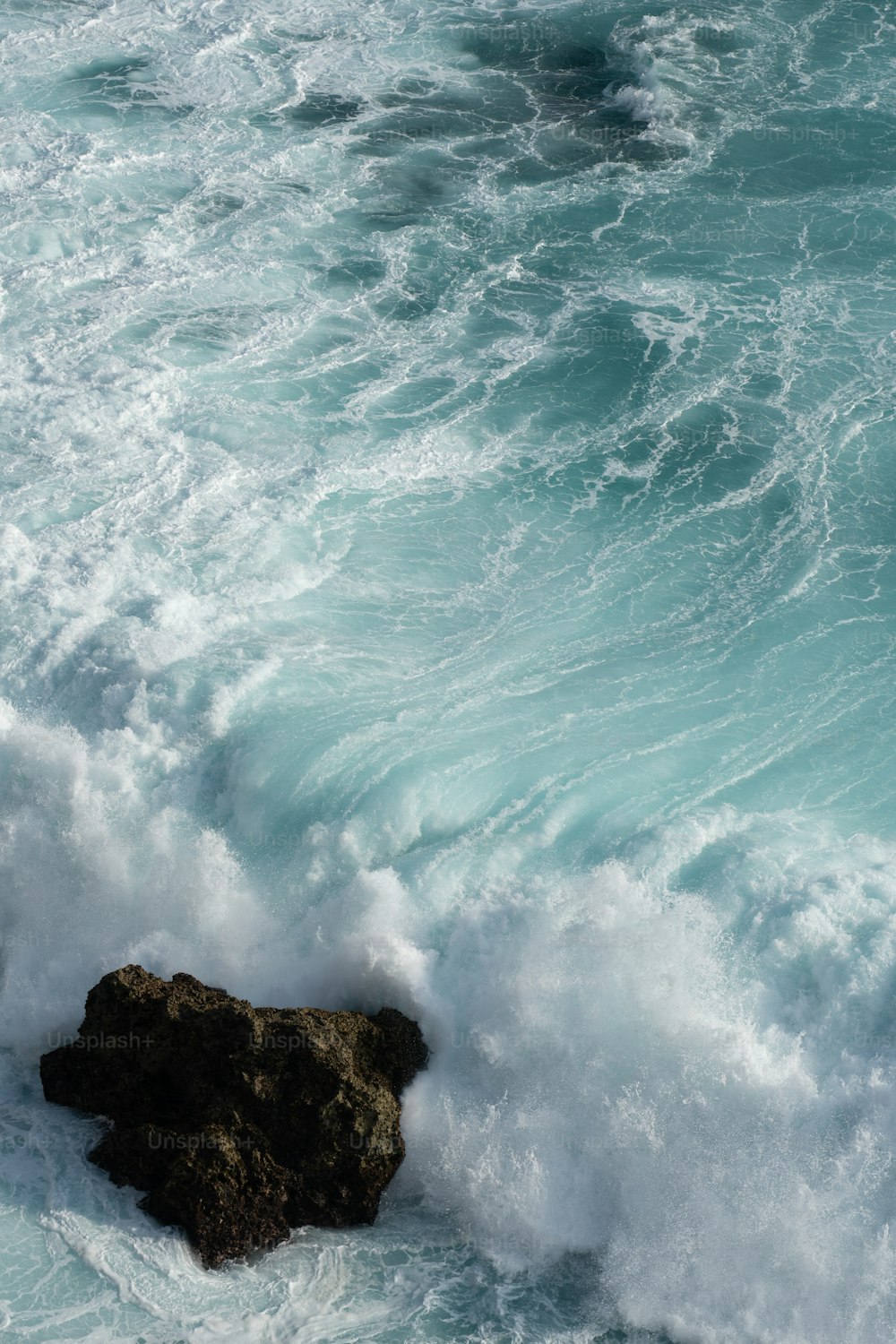 a rock sticking out of the ocean next to a wave