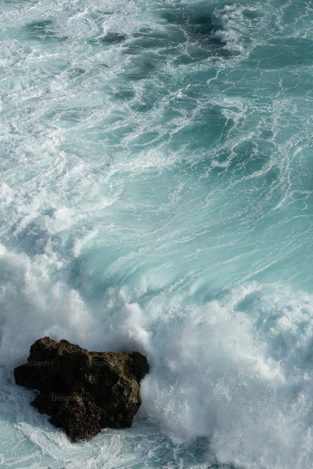 Una roccia che spunta dall'oceano accanto a un'onda