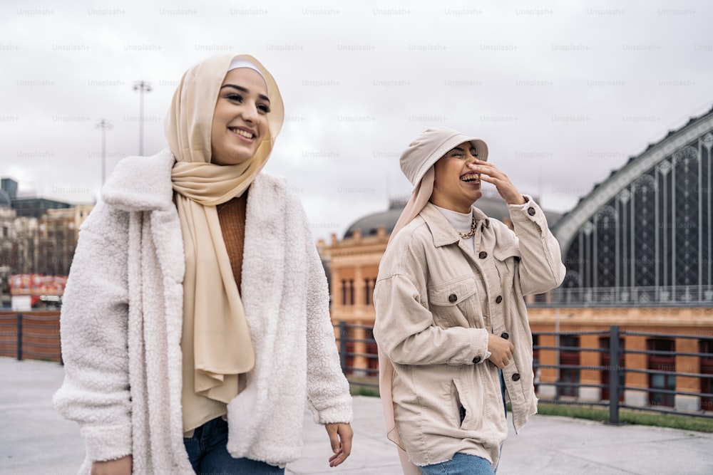 Moças alegres usando hijab rindo e andando na rua.