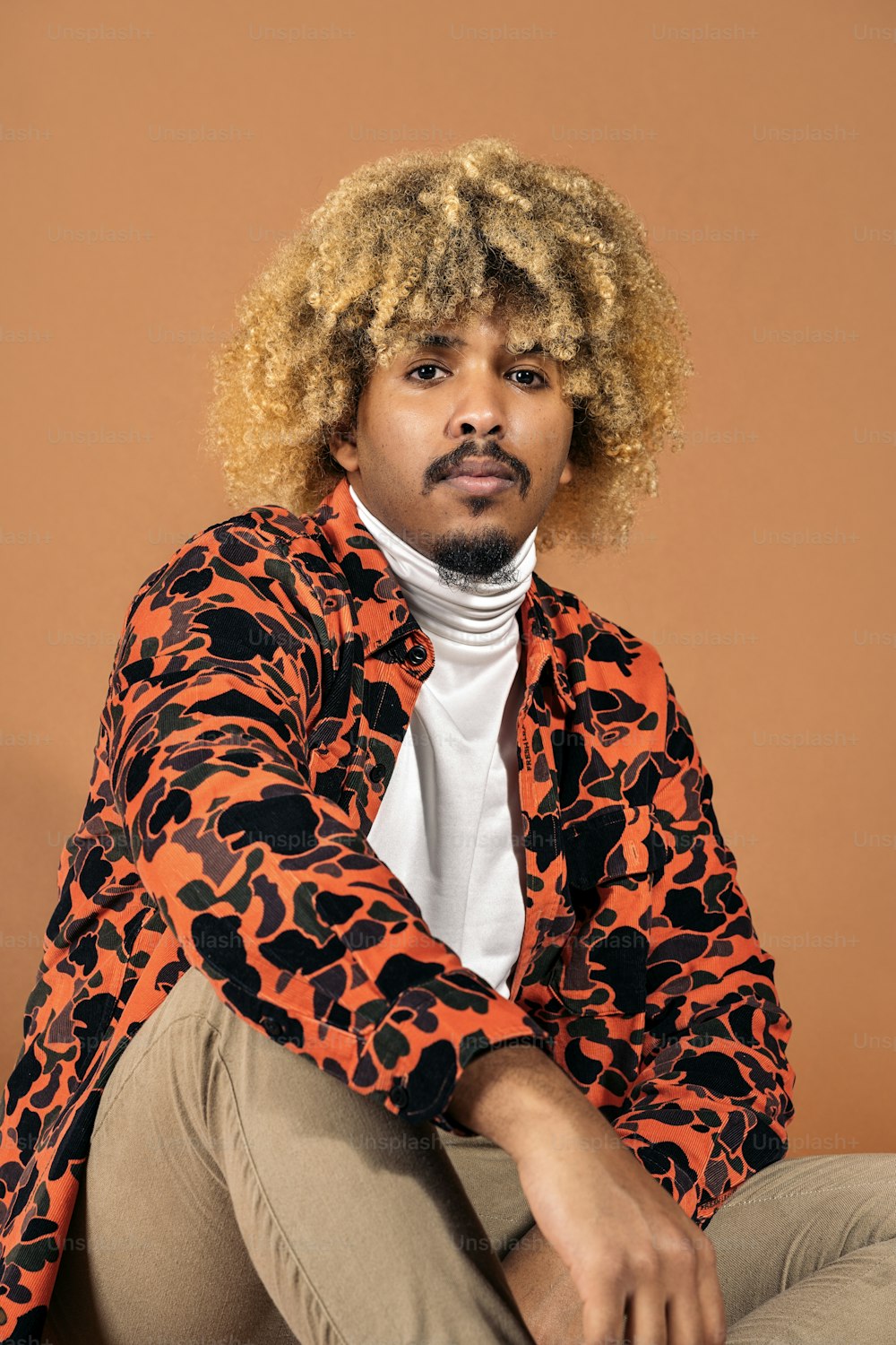 Stockfoto des stilvollen Afro-Mannes, der im Studio vor braunem Hintergrund in die Kamera schaut.