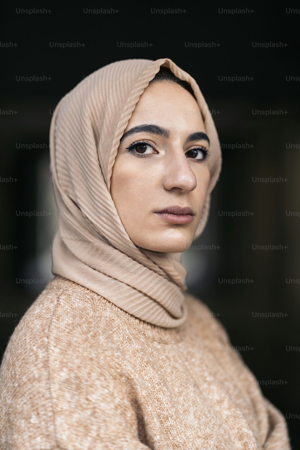 Schöne junge muslimische Frau, die Hijab trägt und draußen in die Kamera schaut.