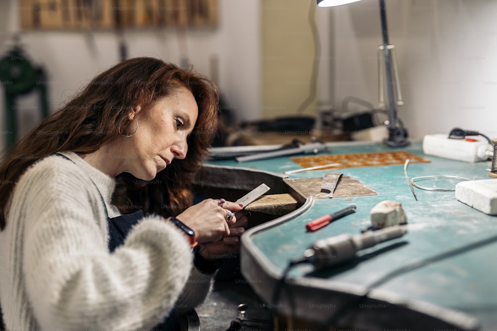 Foto de archivo de mujer concentrada trabajando en el taller de joyería.