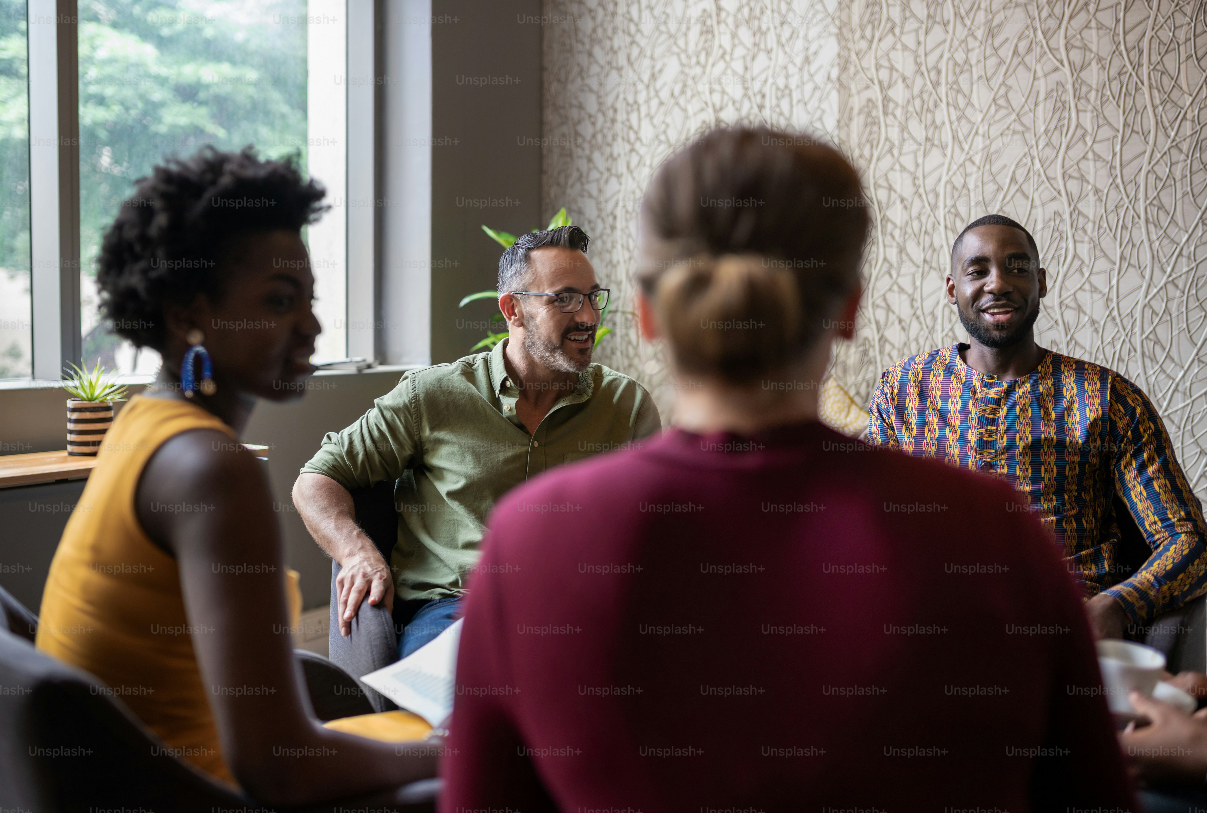 Groupe diversifié d’hommes d’affaires souriants assis ensemble dans le salon d’un bureau et discutant de travail