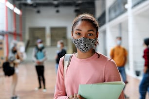 Ritratto di studente afroamericano con maschera facciale al college o all'università, concetto di coronavirus.